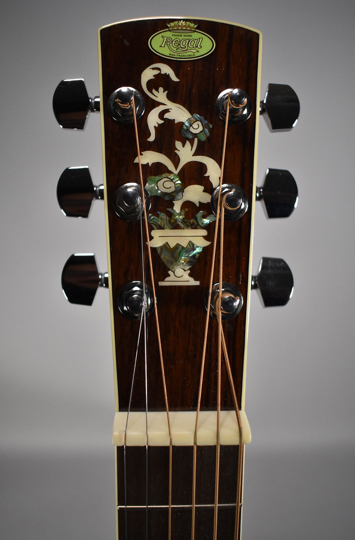 Close-up of the dark wood headstock with a mother-of-pearl floral inlay, six chrome tuners, and a white nut.