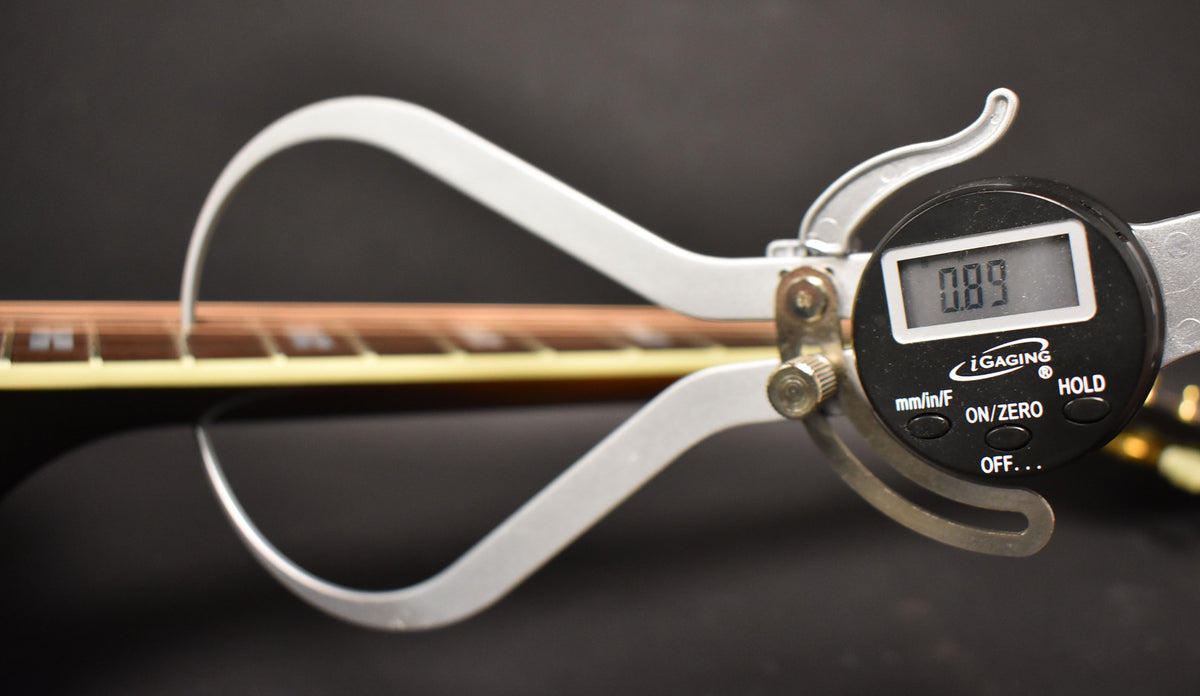 A digital caliper measures the guitar's fret height at 0.89, with the dark sunburst body and light binding visible below.