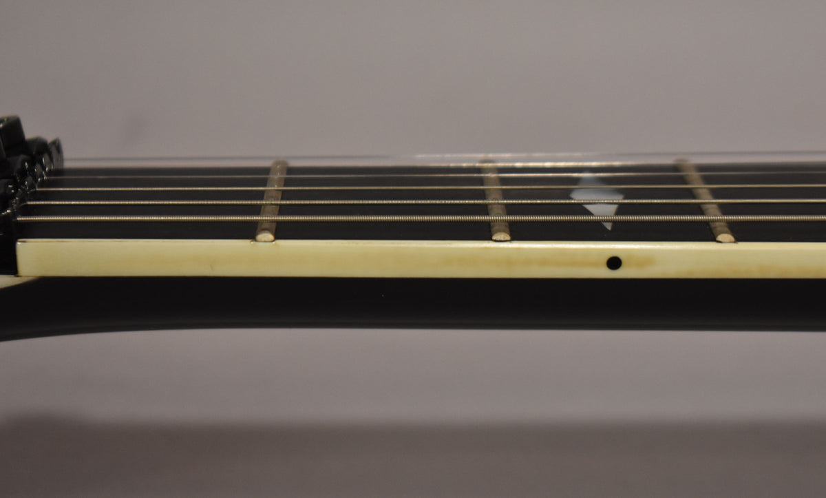Close-up of the black fretboard and cream binding, showing a pearloid diamond inlay and a black side dot marker.