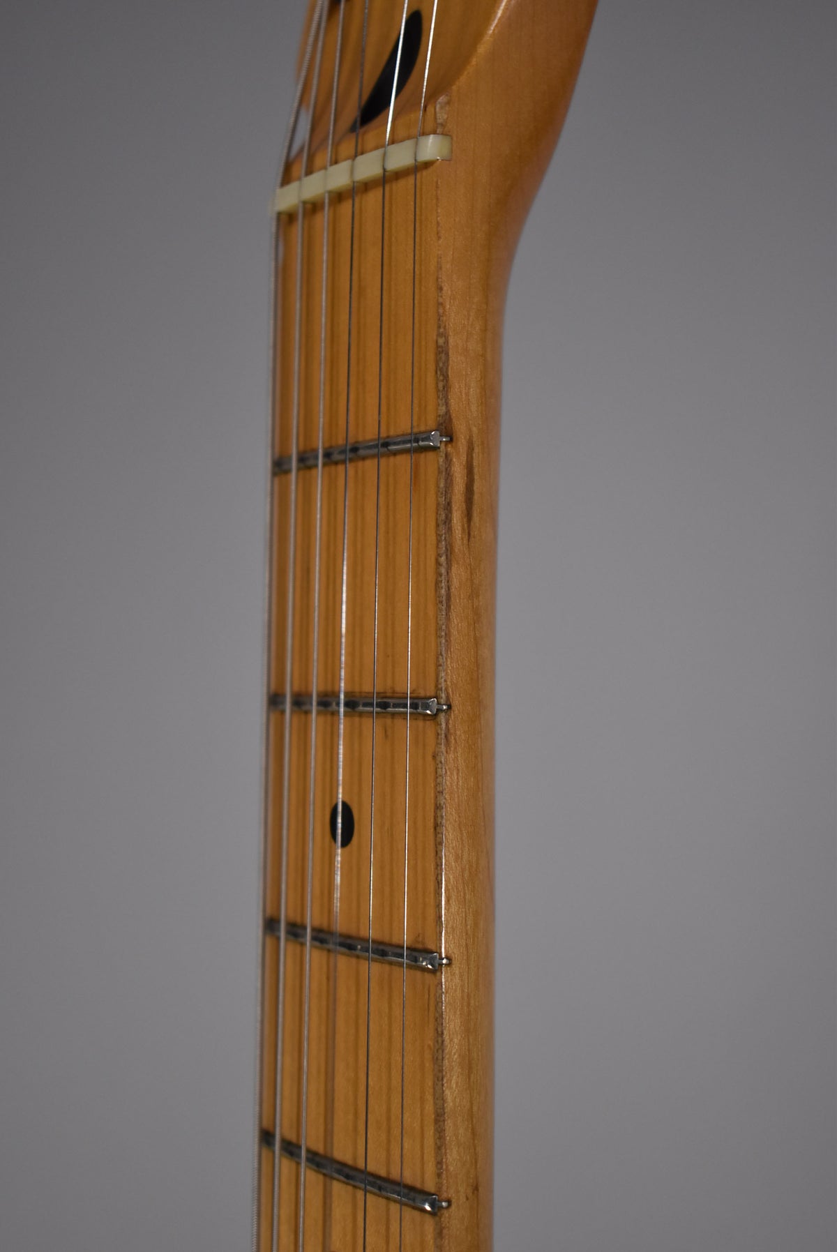Close-up of the maple neck and fretboard, showing a worn satin finish, dark fret markers, and a cream nut.