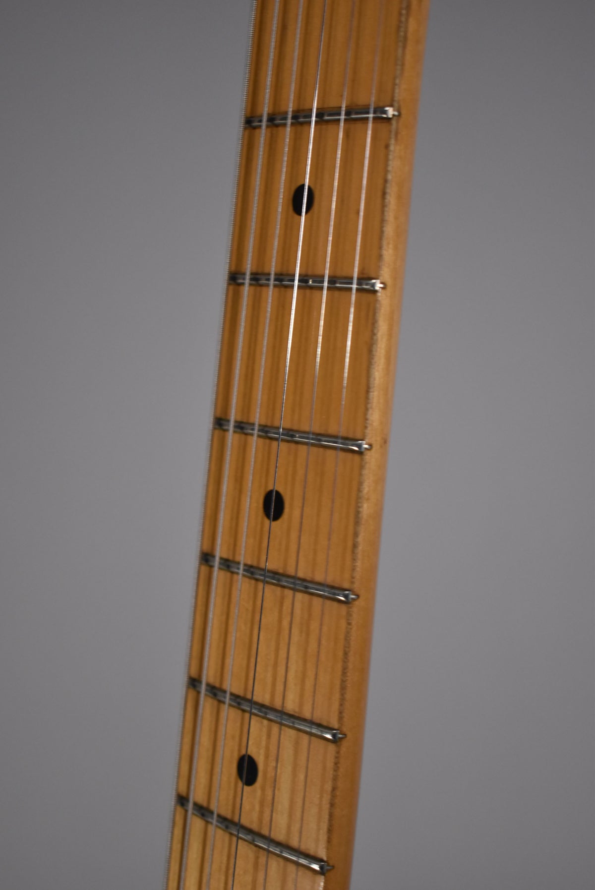 Close-up of the maple fretboard, angled right, showing black dot inlays, frets, and strings, with some wear visible on the fret edges.