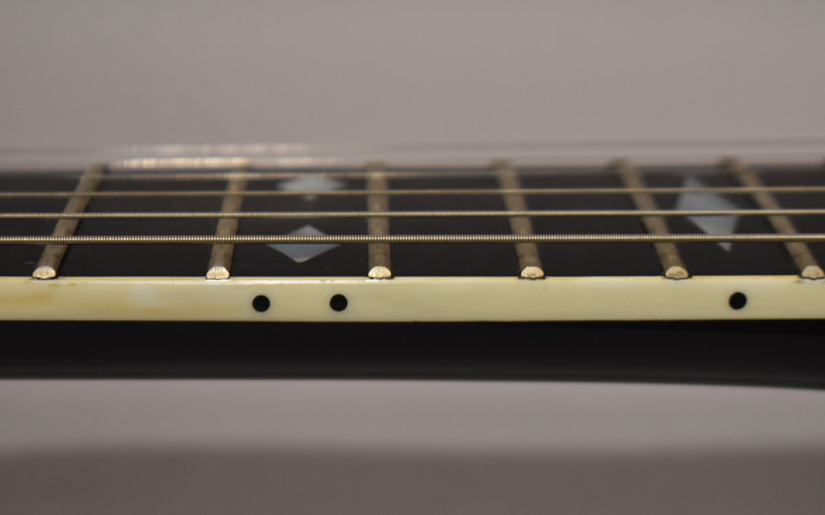 Close-up of the black fretboard with diamond inlays, showing light wear on the frets and cream binding with black side dots.