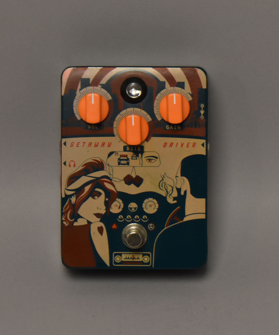 Overhead view of a pedal with a retro graphic of a couple in a car, featuring three orange knobs and a silver footswitch.