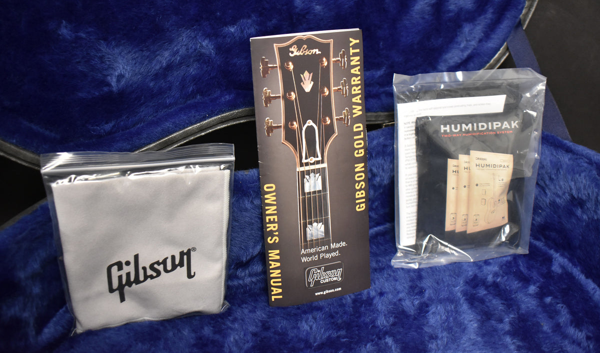 Accessories: a white polishing cloth in a clear bag, an owner's manual, and a Humidipak system, all on a blue plush case lining.