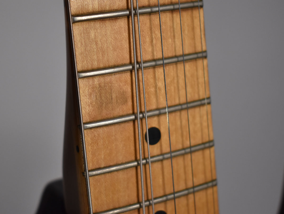 Close-up of the maple fretboard and frets, showing dark circular inlays and light wear on the frets.