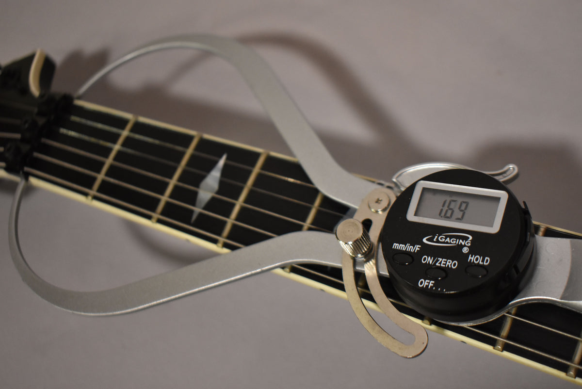 A digital fret height gauge shows 1.69mm on the black fretboard with white diamond inlays and cream binding.