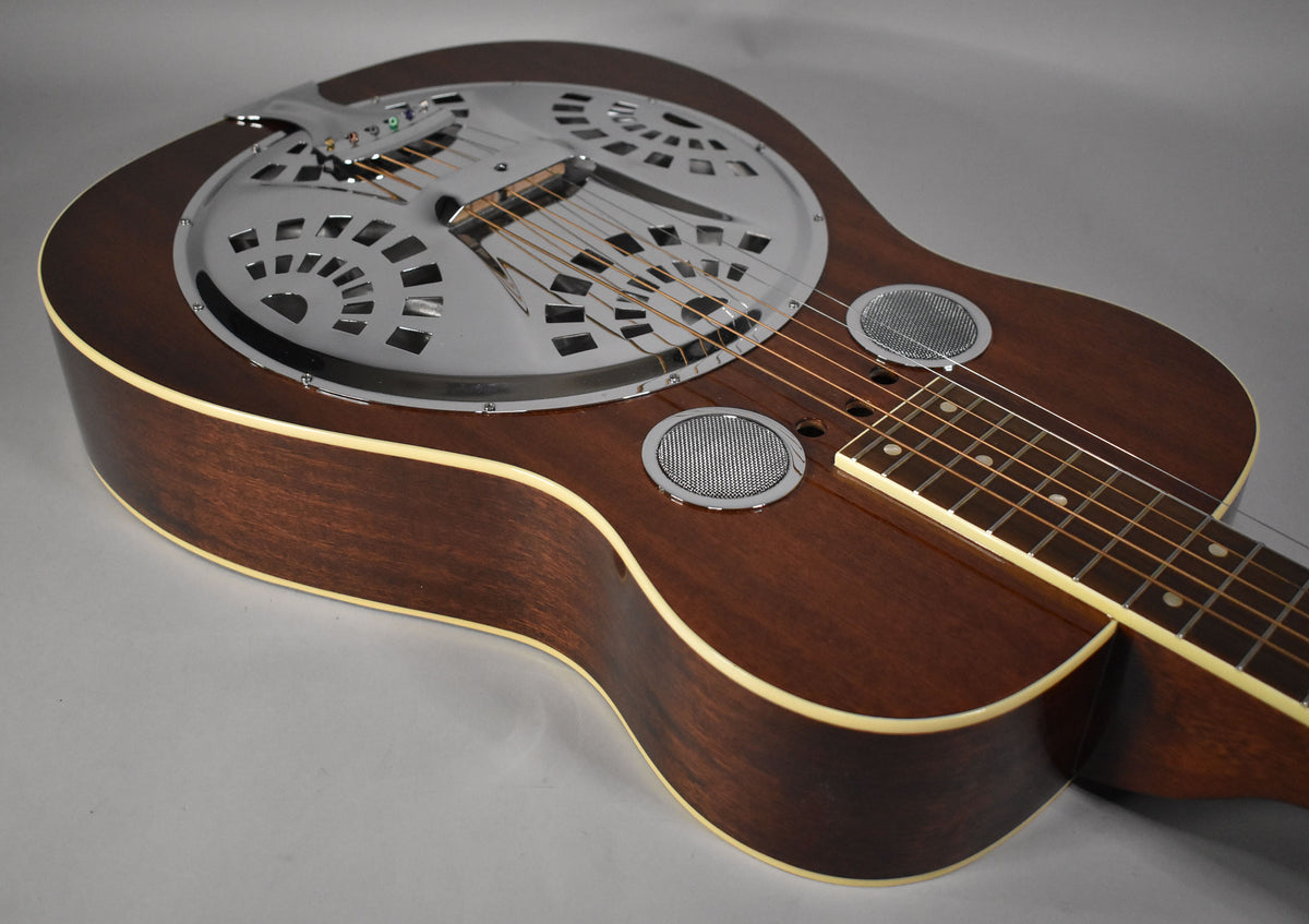 A dark brown resonator guitar, angled from the upper left, shows its chrome resonator cone, two round sound holes, and light binding.