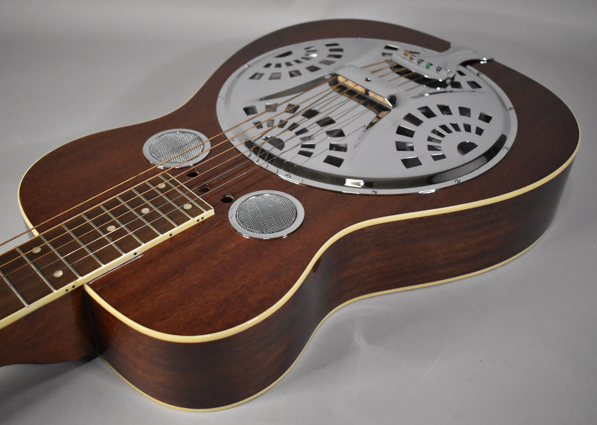 The dark brown resonator guitar is angled from the left, showing its chrome resonator cone, two round sound screens, and binding.
