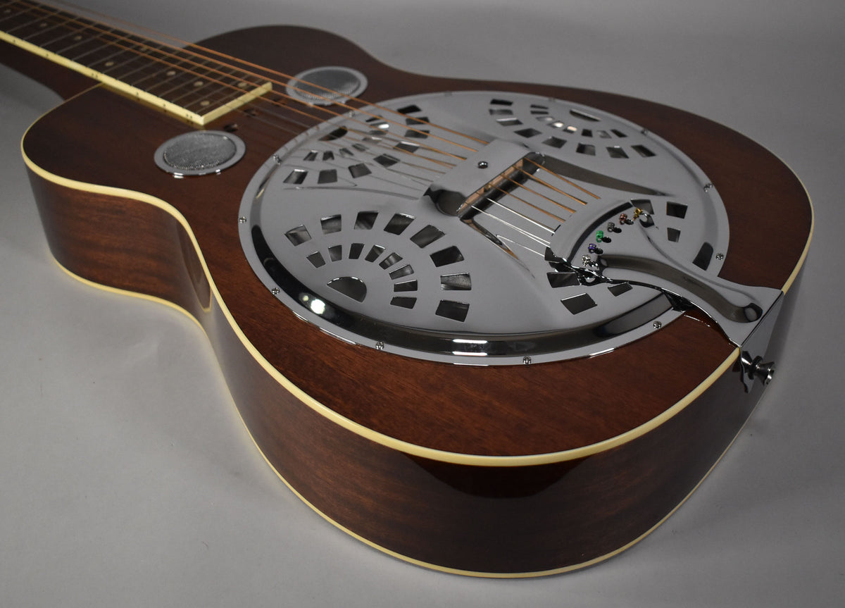 The dark brown resonator guitar, with a natural gloss finish and cream binding, is angled to show its chrome cover plate.
