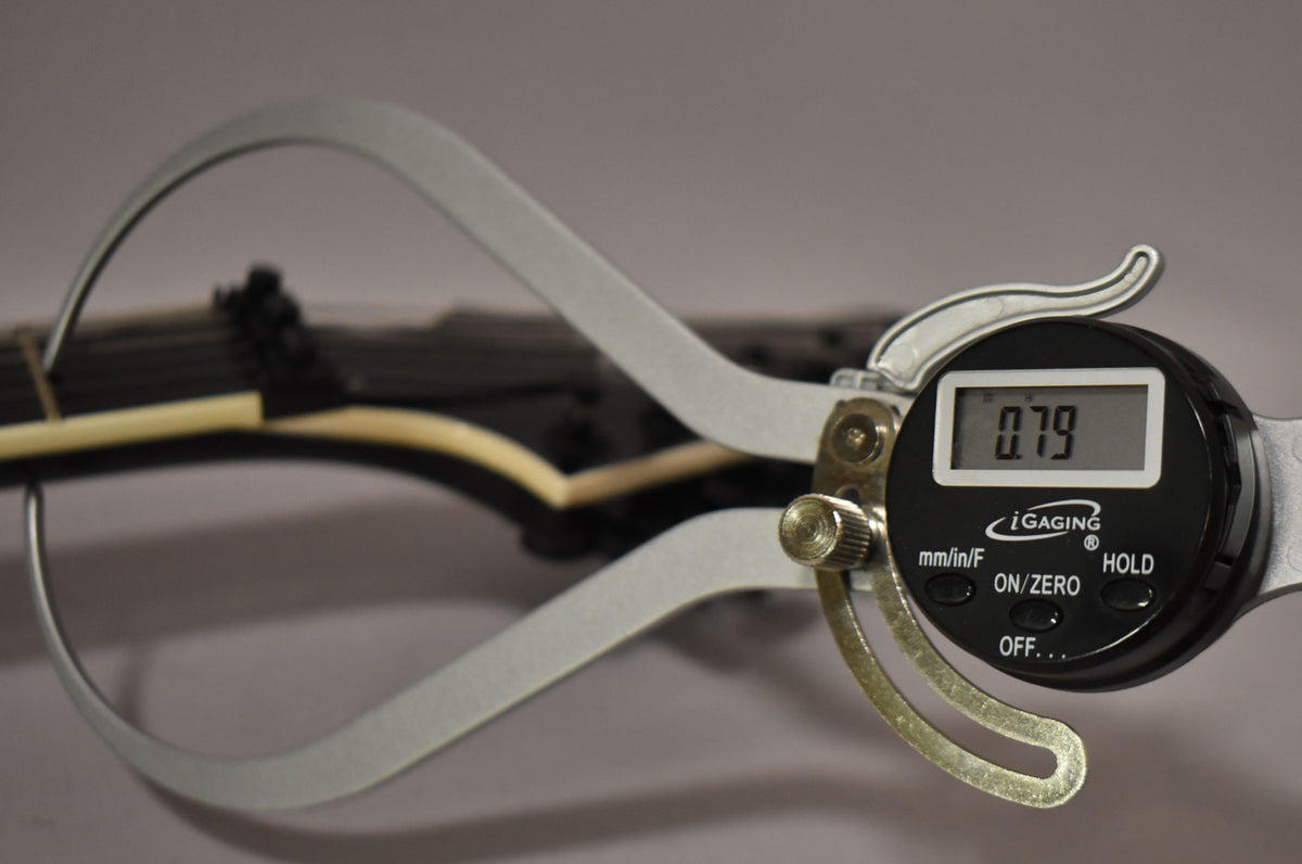 A digital caliper measures the black guitar's fretboard, showing 0.79 on its screen.