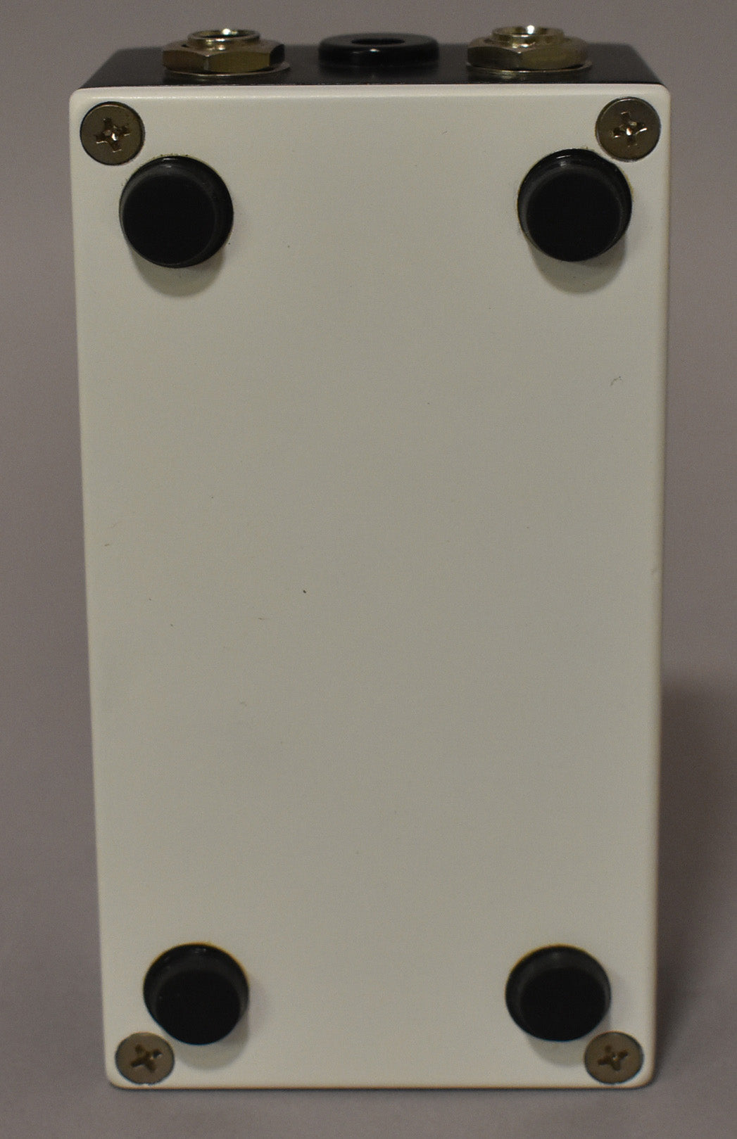 The pedal's off-white underside is visible, showing four black rubber feet and four gold-colored screws, with some minor scuffs.