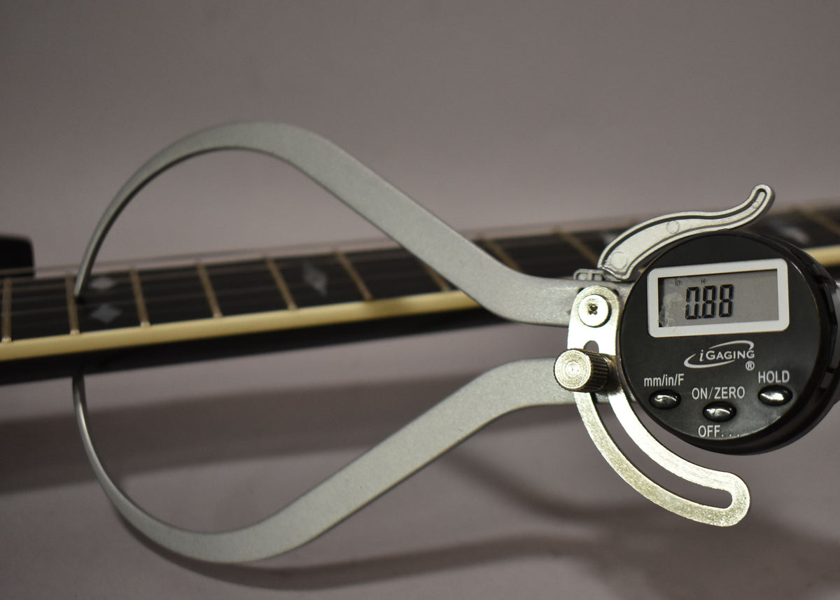 A digital caliper measures the black fretboard with diamond inlays, showing a reading of 0.88.