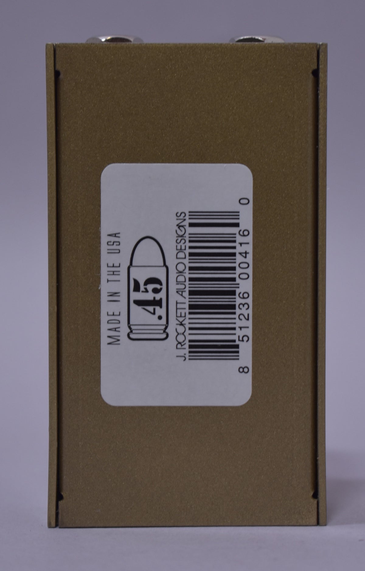The pedal's gold-tan textured side is shown, with a white barcode sticker featuring a bullet graphic and product information.