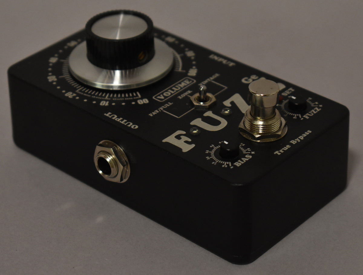 Black effect pedal, angled from the left, showing a large silver-capped volume knob, two mini-knobs, and a footswitch.
