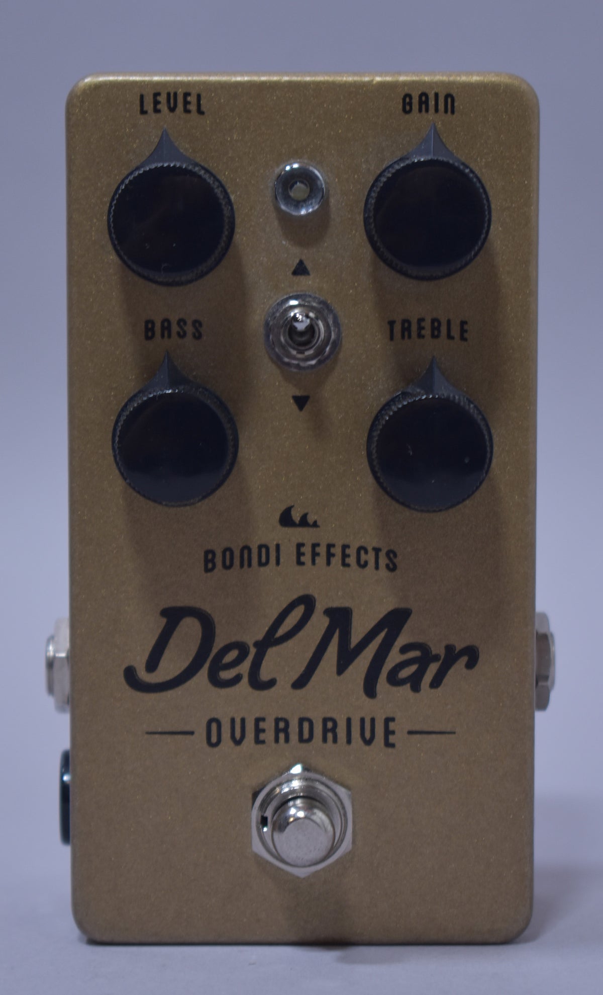 The gold sparkle pedal is seen from above, featuring four black knobs, a toggle switch, and a footswitch, all with minor wear.
