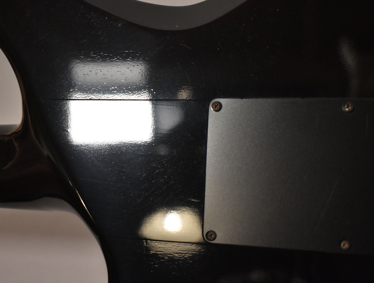 Close-up of the guitar's glossy black back, showing light scratches and a matte black control cavity cover secured by four screws.
