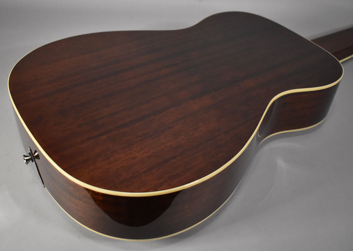 The back of the dark brown resonator guitar, with a natural gloss finish and cream binding, is angled to show the strap button.