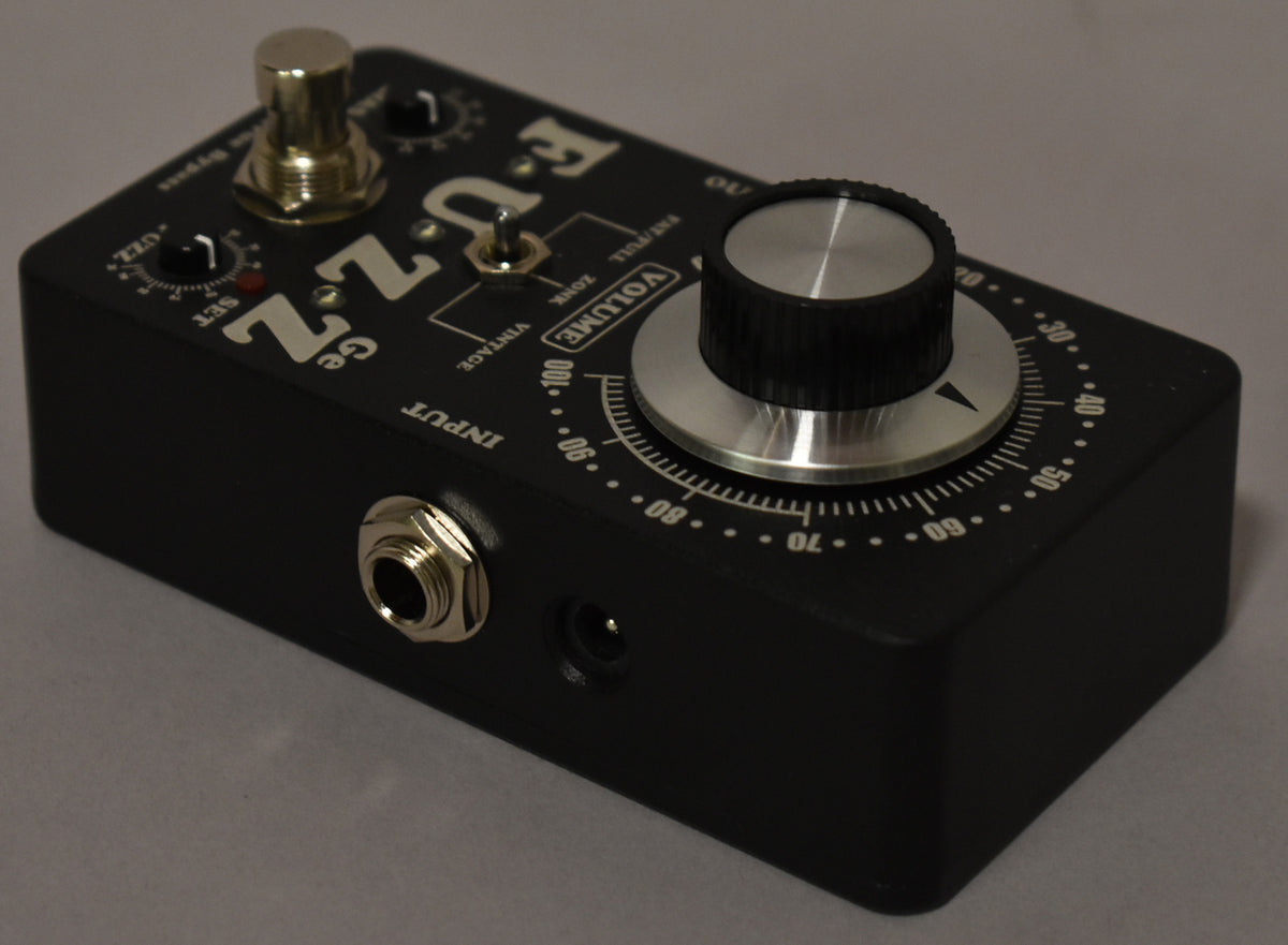 A black fuzz pedal, angled from the front-left, showing a large silver volume knob, two smaller knobs, and an input jack.