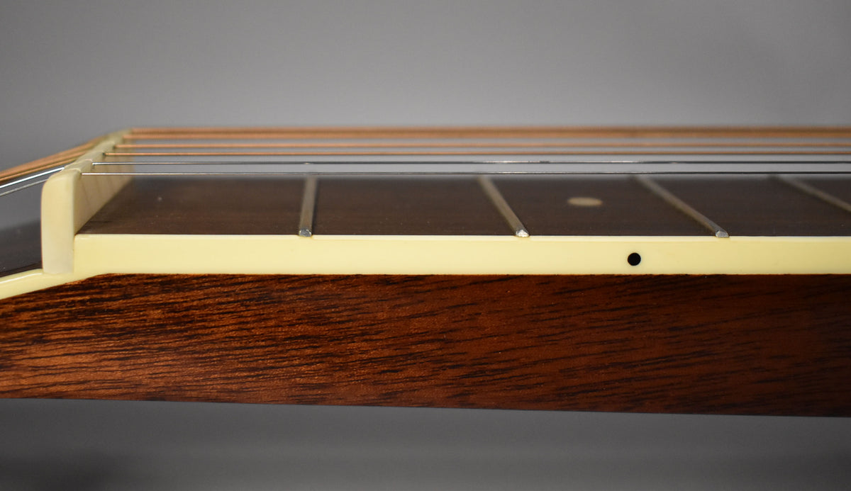 Close-up of the dark brown fretboard and light cream binding, showing the low action of the strings and a single black dot inlay.
