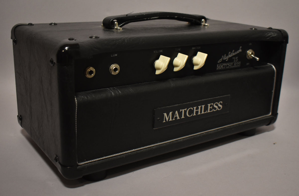 The black amplifier head is angled from the right, showing the front panel with two inputs, three cream knobs, and a toggle switch.