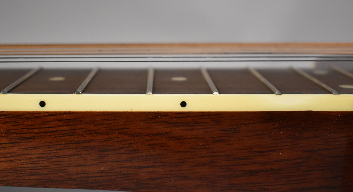 Close-up of the dark wood fretboard and light binding, showing the frets, strings, and two small black side dots.