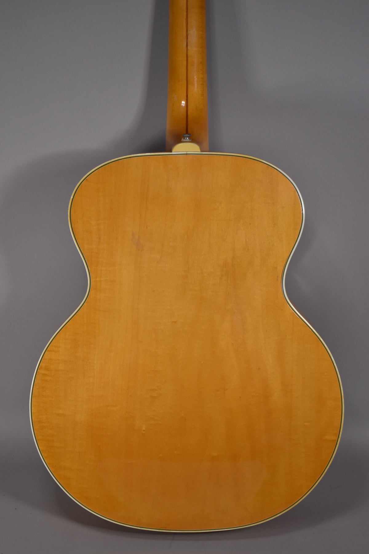 The guitar's blonde back and neck are visible from behind, showing light wood grain and a few small indentations.
