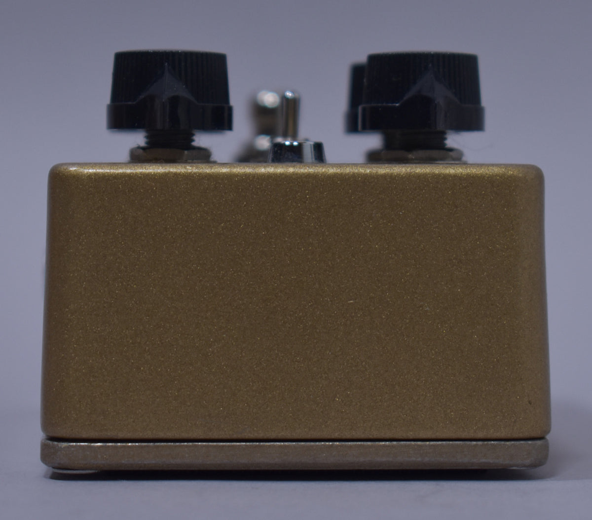 The gold sparkle effect pedal is viewed from the side, showing two black pointer knobs and a chrome toggle switch on top.
