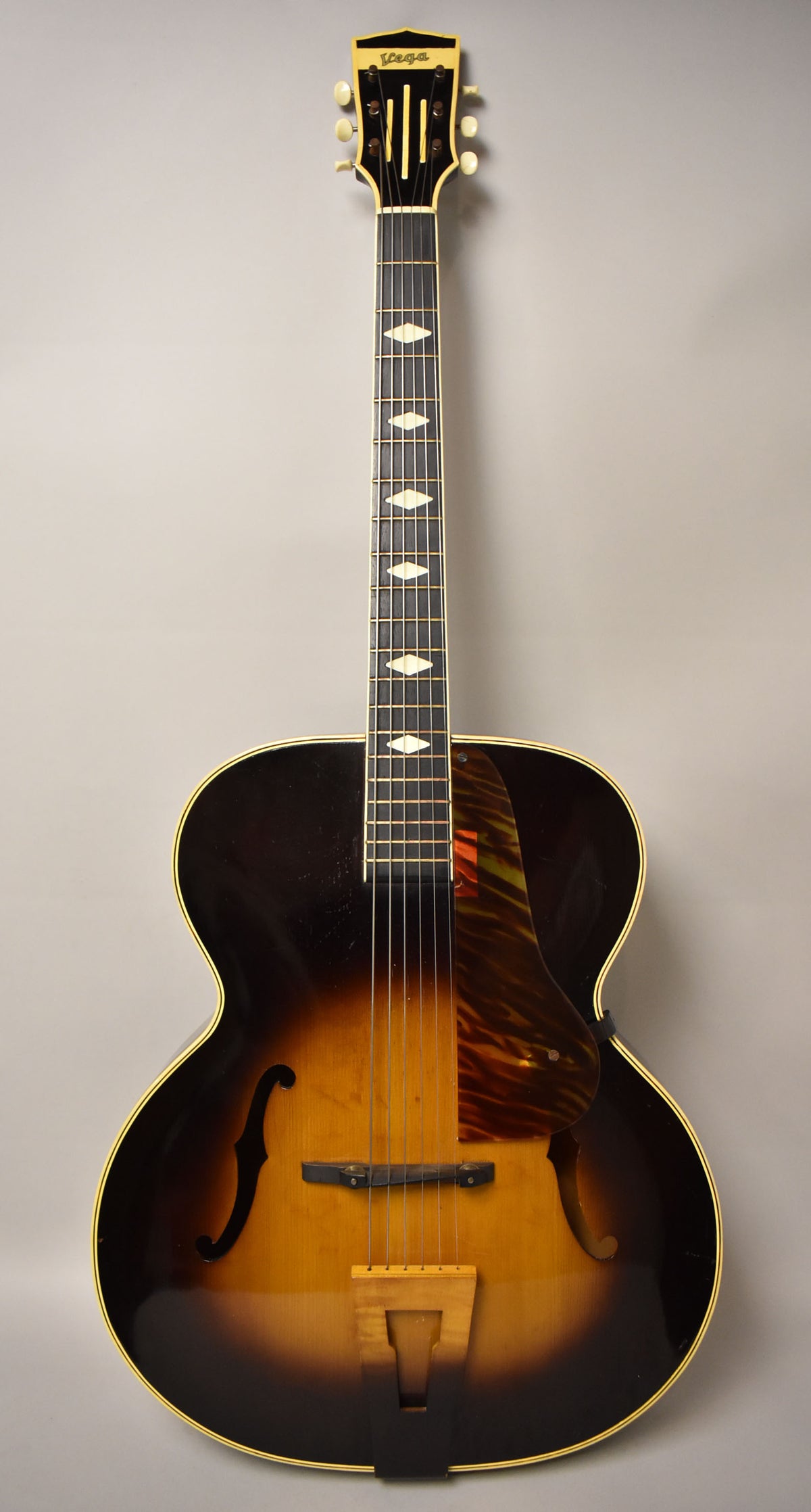 Full front view of a sunburst archtop acoustic guitar with f-holes, a tortoiseshell pickguard, and diamond fretboard inlays.