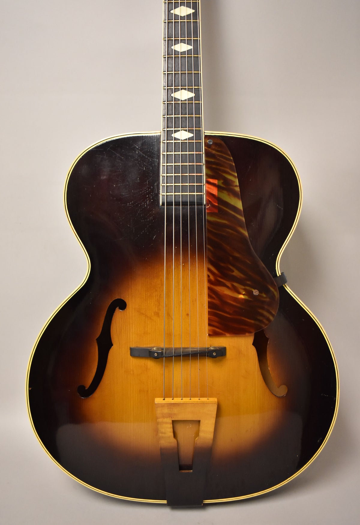Full-frame view of the sunburst archtop's body and lower neck, showing f-holes, a tortoise pickguard, and visible finish wear.