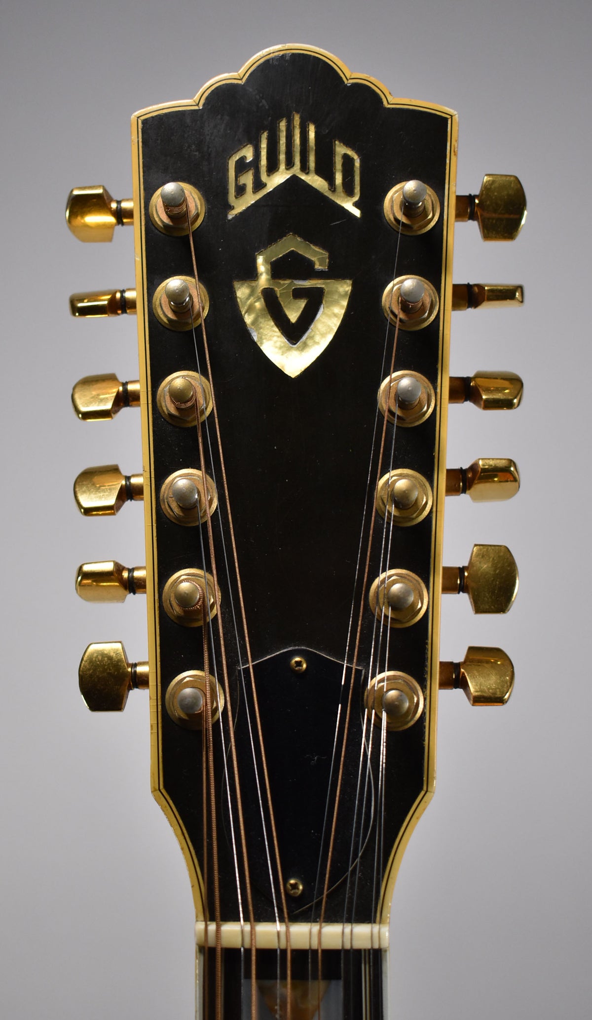 Close-up of the black headstock with gold tuners, showing some finish wear and a gold inlaid logo.
