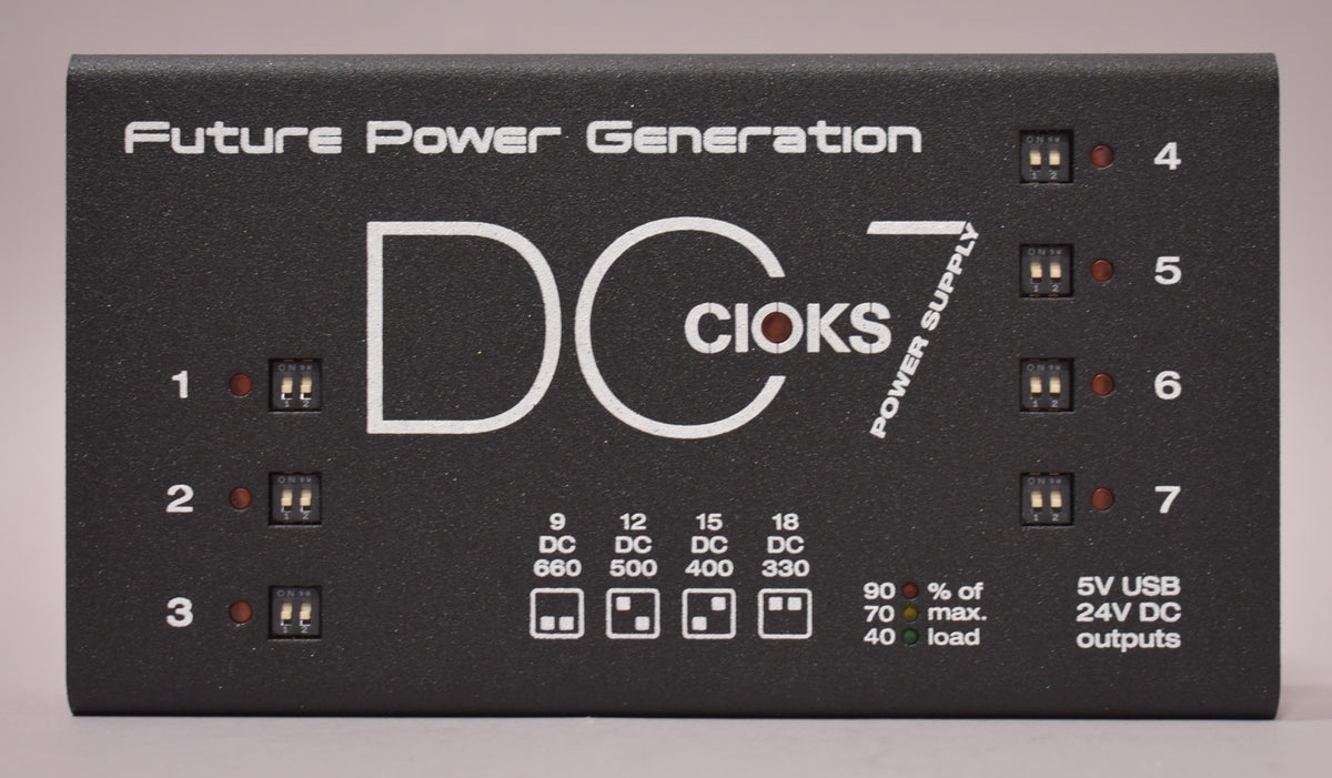 The black textured power supply is viewed from above, showing seven numbered outputs with small red indicator lights and dip switches.