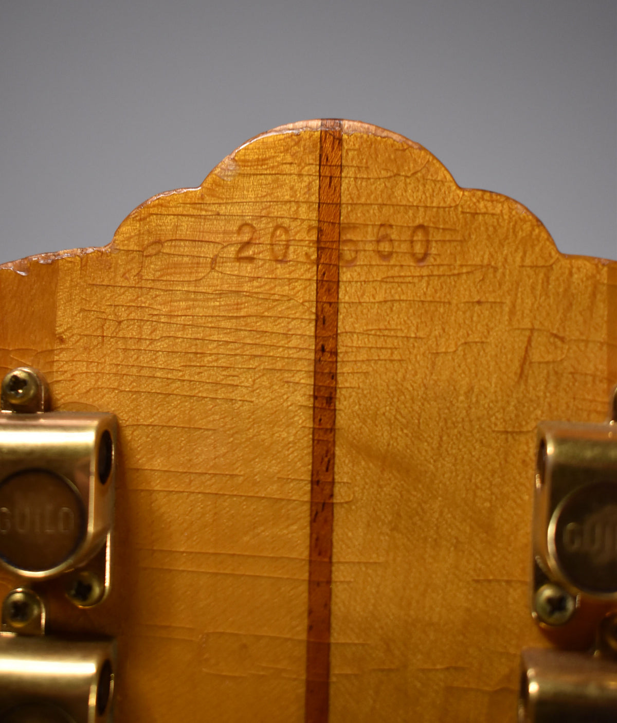 Close-up of the blonde headstock back, showing a vertical dark wood stripe, serial number "203560", and gold tuners.