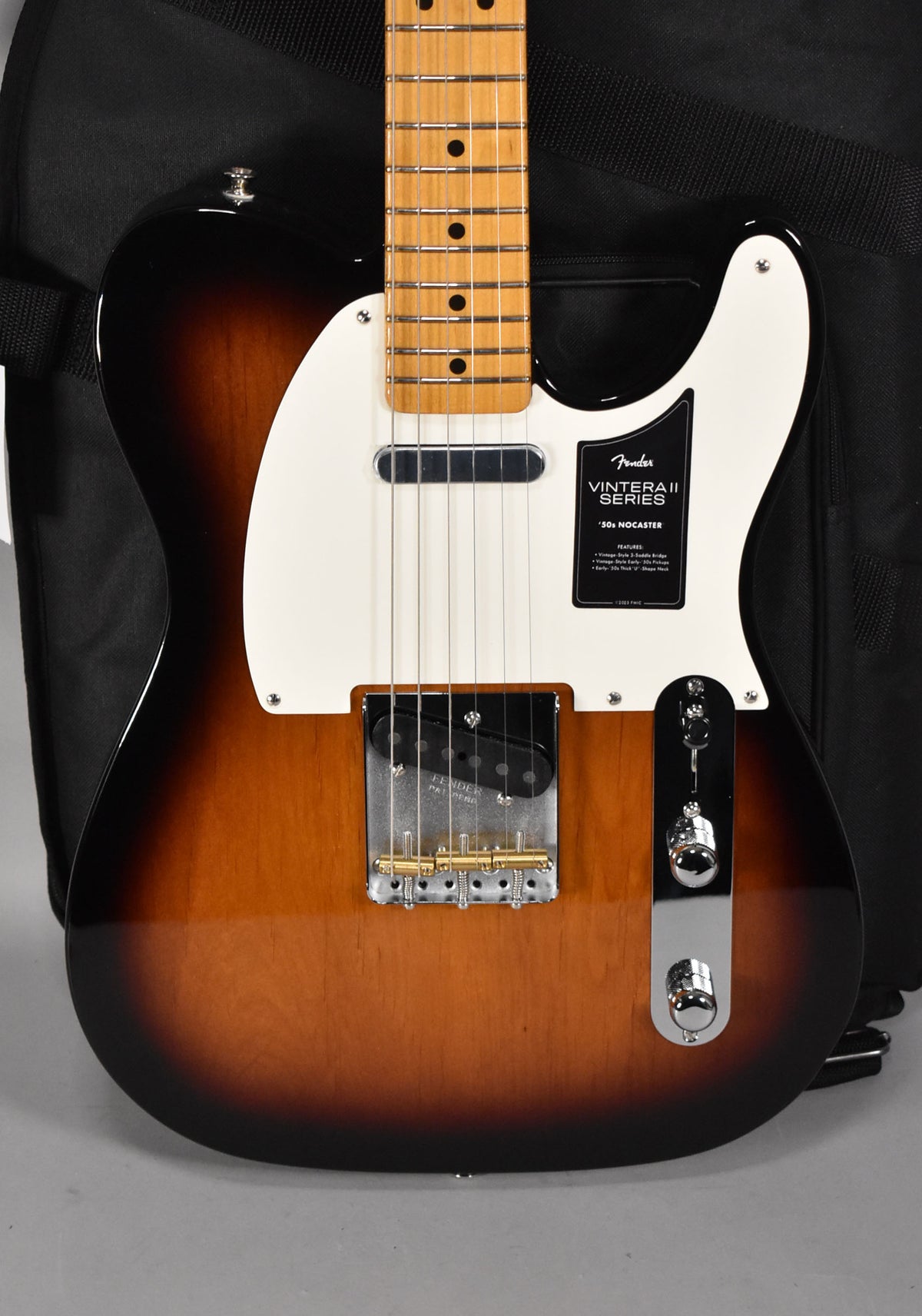The electric guitar's sunburst body, white pickguard, and maple fretboard are framed from the upper bout to the lower controls.