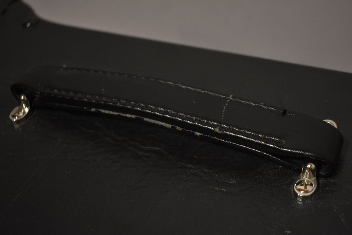Close-up of the black leather handle, showing wear and scuffing along the edges and two silver-colored metal end caps.