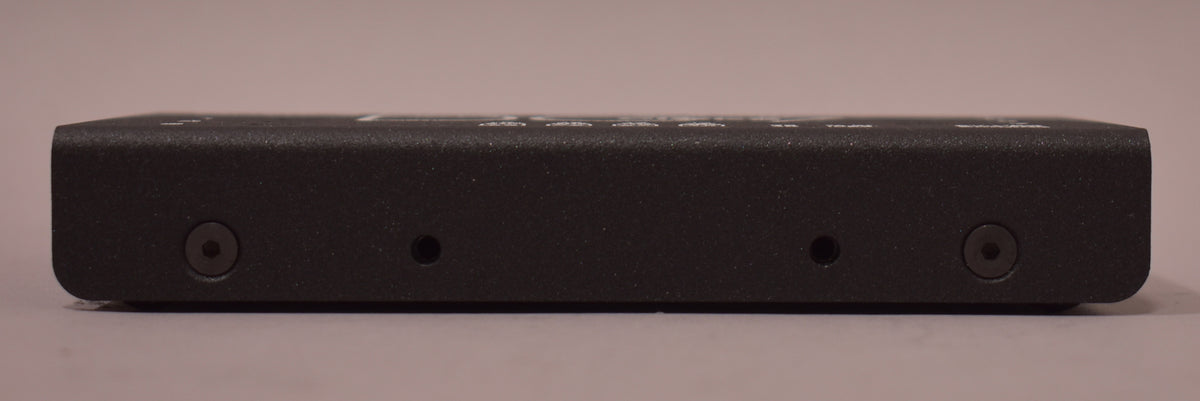 The black textured power supply is viewed from the side, showing two hex screws and two small holes on its face.
