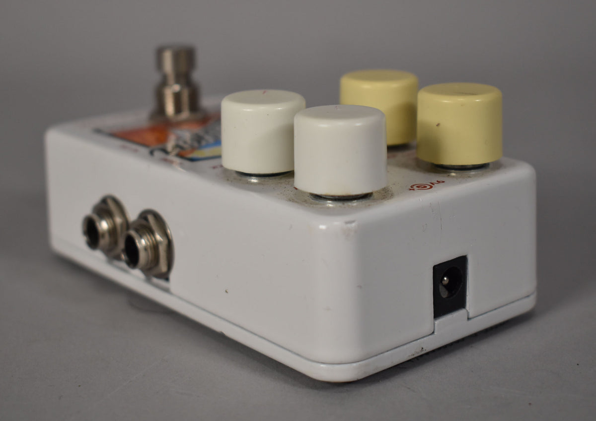 The white pedal is angled right, showing two input jacks, a power input, and four control knobs, two white and two yellow.