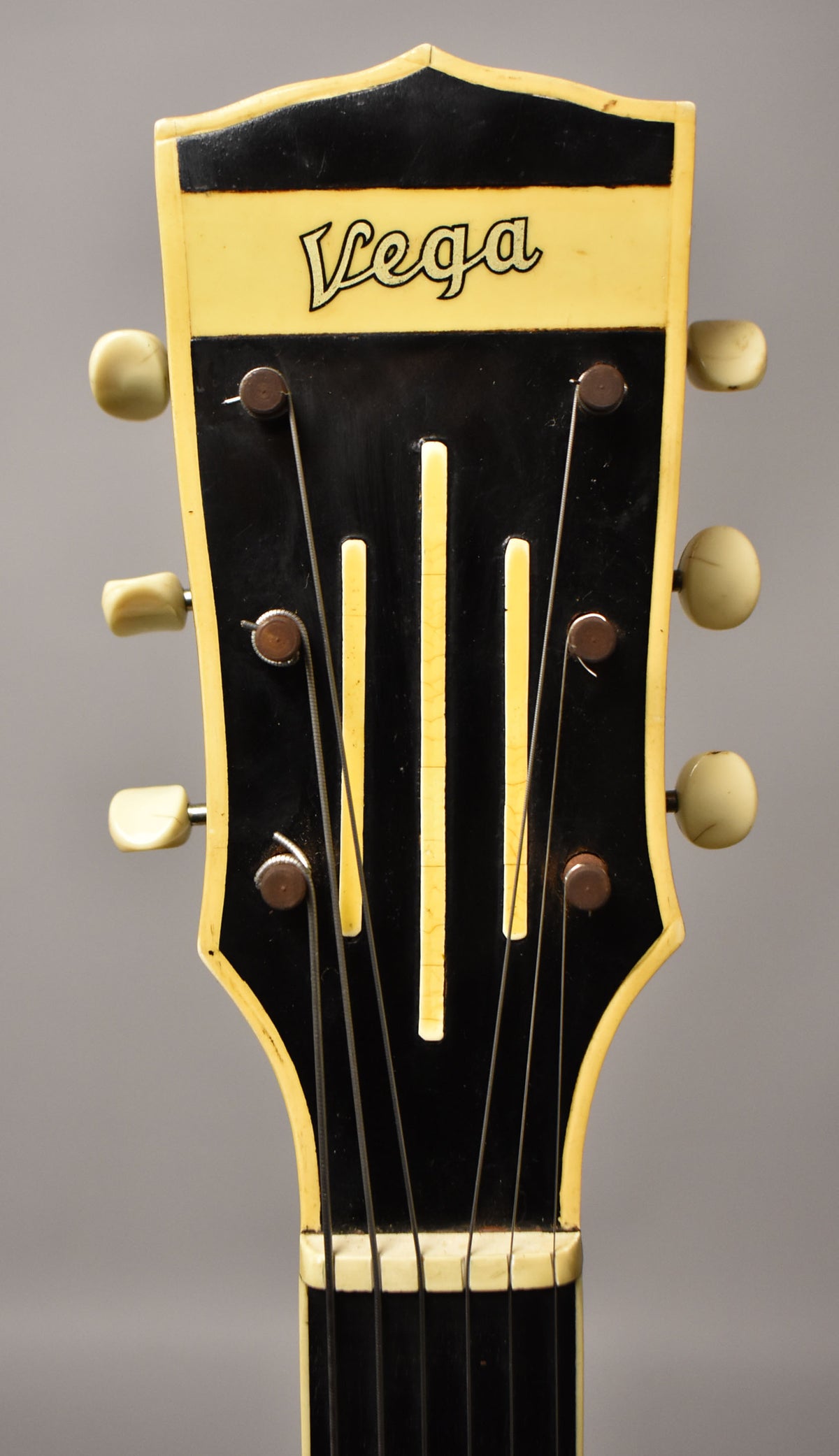 Close-up of the guitar's headstock, showing a black face with a cream border, cream tuning pegs, and visible finish checking.