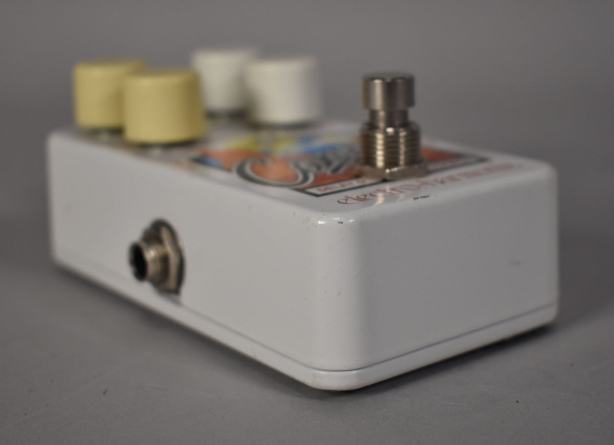 A white pedal with a colorful graphic top, four cream and white knobs, a silver footswitch, and a side input jack.