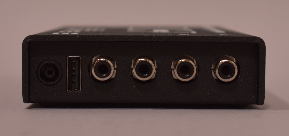 The black power supply's back edge is framed, showing a power input, a USB-A port, and four silver-ringed output jacks.