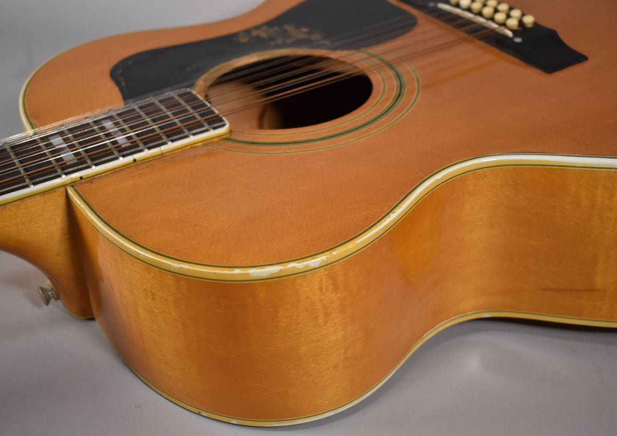 The natural blonde jumbo 12-string acoustic guitar is angled to show its lower bout, with finish wear along the binding.