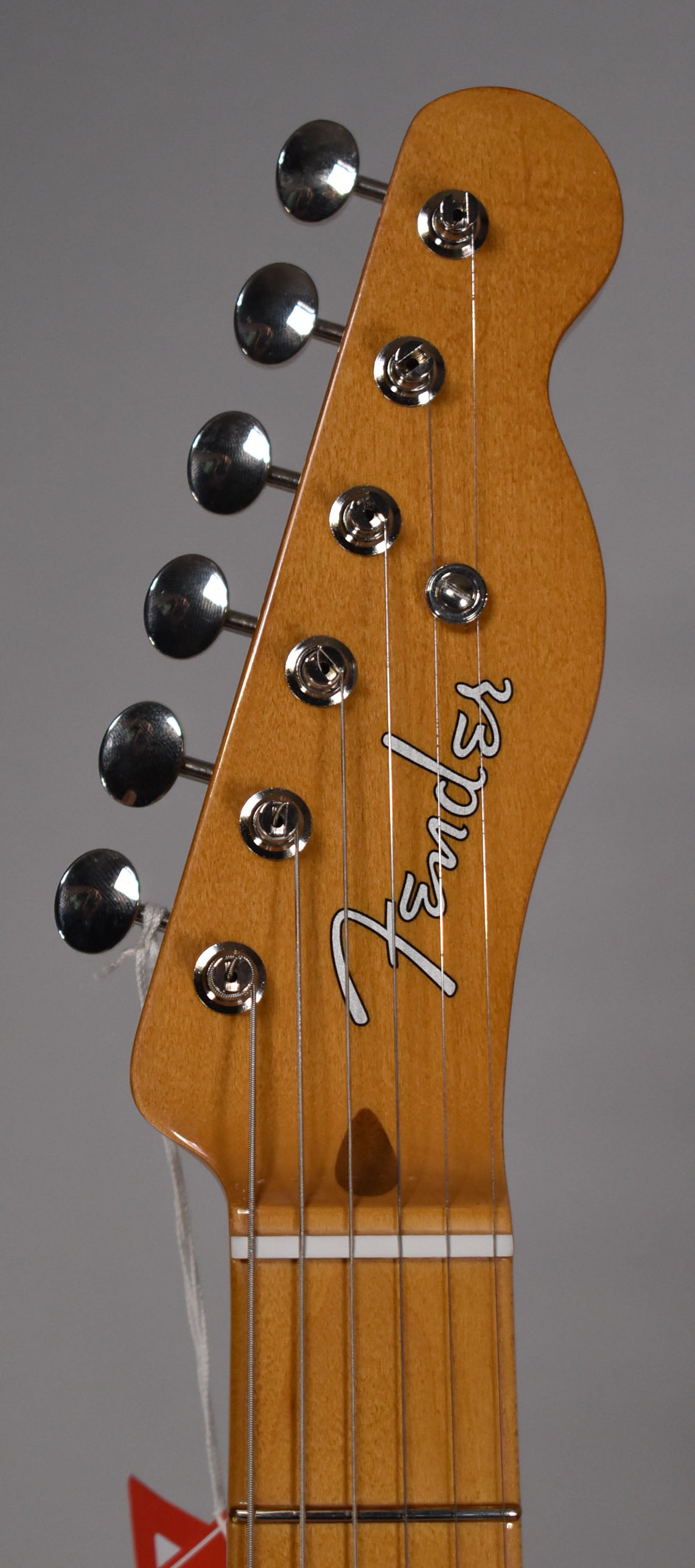 Close-up of the guitar's headstock, angled slightly left, showing six chrome tuning pegs and the light brown wood grain.