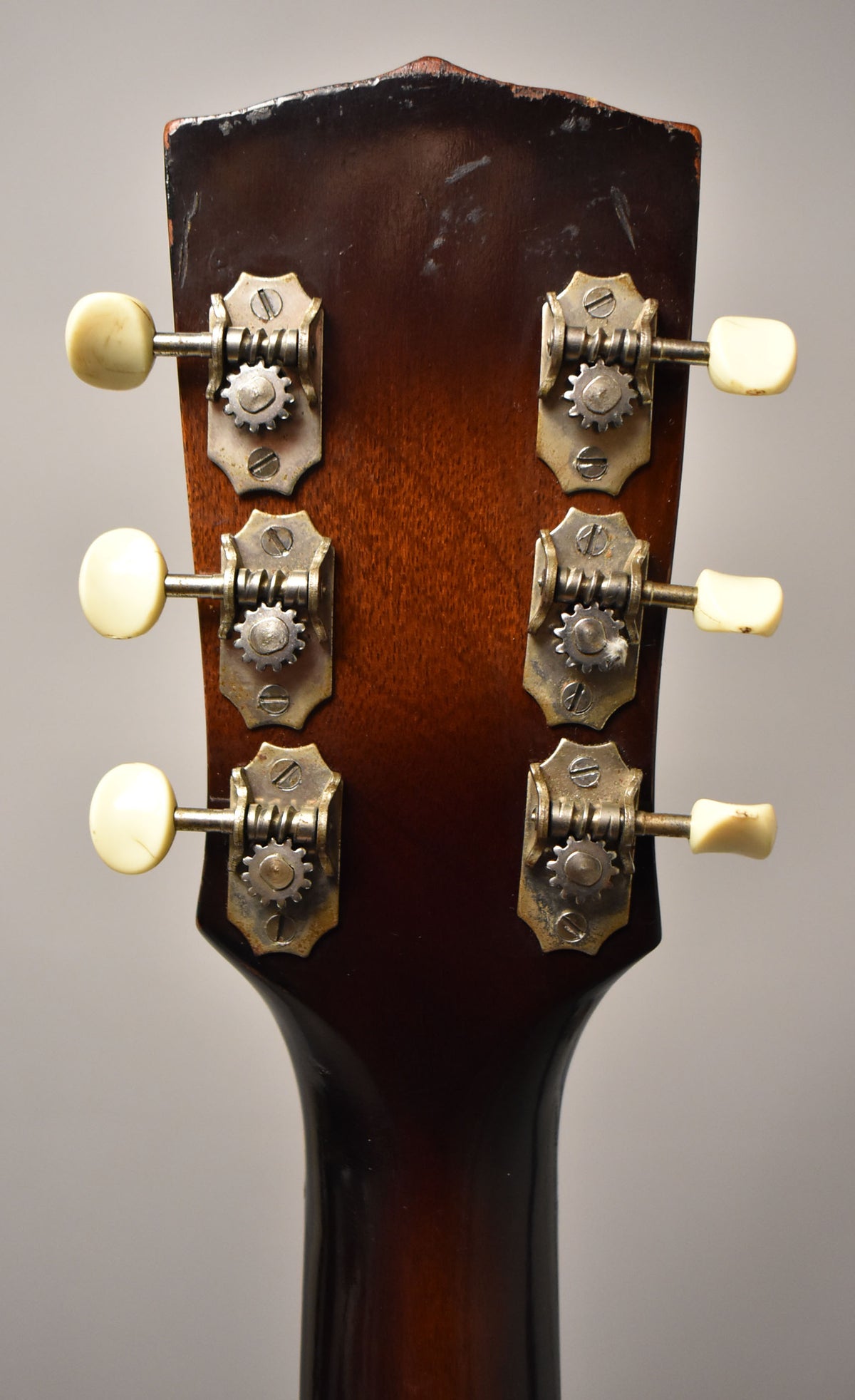 The guitar's dark sunburst headstock, viewed from the back, shows six cream tuning pegs with tarnished open-gear tuners.