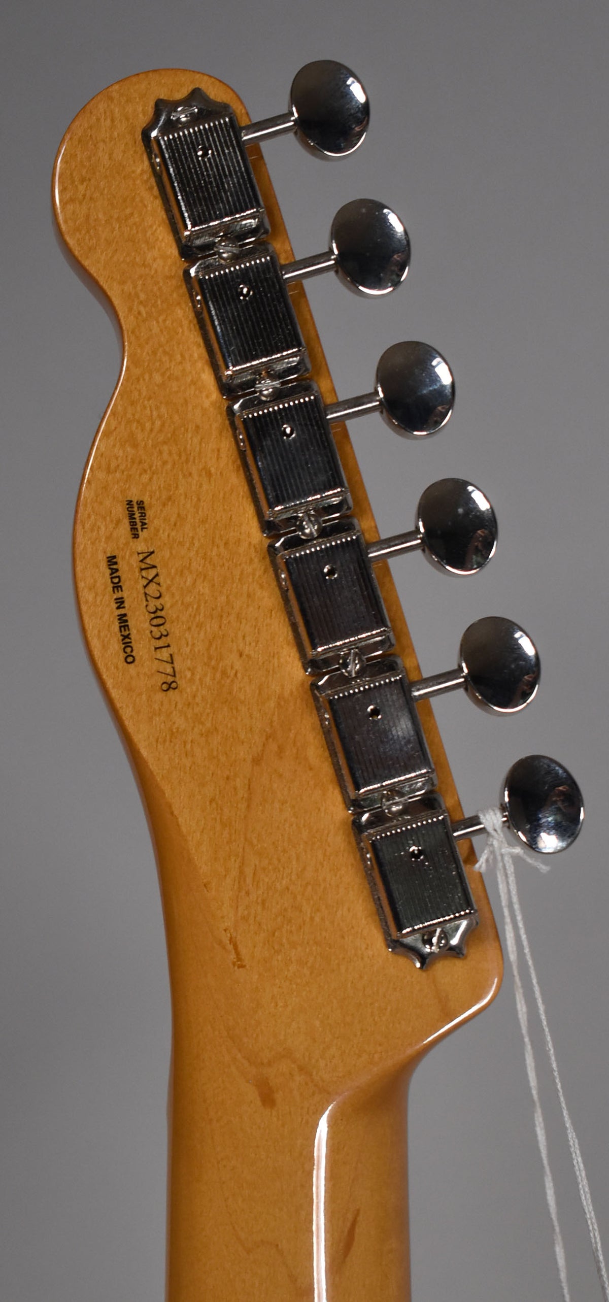 The back of a light brown guitar headstock with six chrome tuners and a white string tied to the lowest tuner.