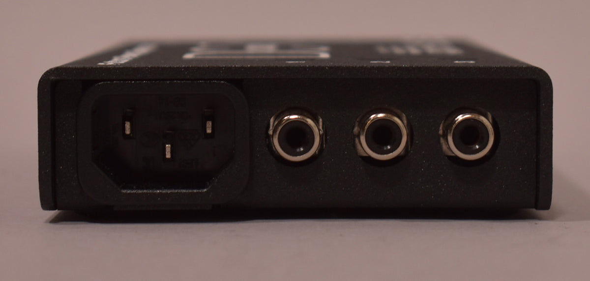 The black textured power supply is viewed from the rear, showing a three-prong power inlet and three silver-ringed output jacks.