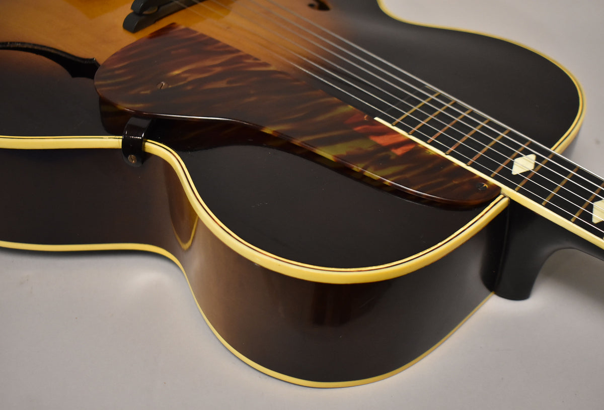Close-up of the sunburst archtop's lower bout, showing the dark brown finish, cream binding, tortoiseshell pickguard, and fretboard with diamond inlays.