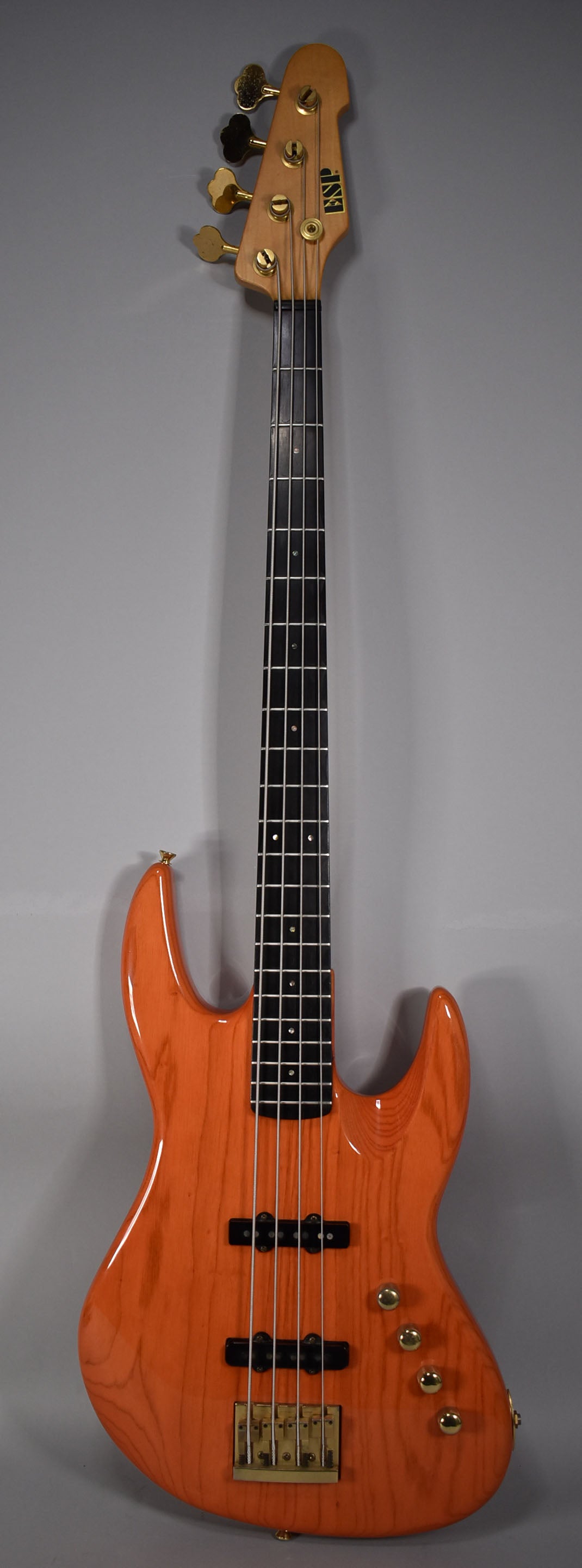 Full-length, front view of a translucent orange bass with a black fretboard, gold hardware, and two black pickups.