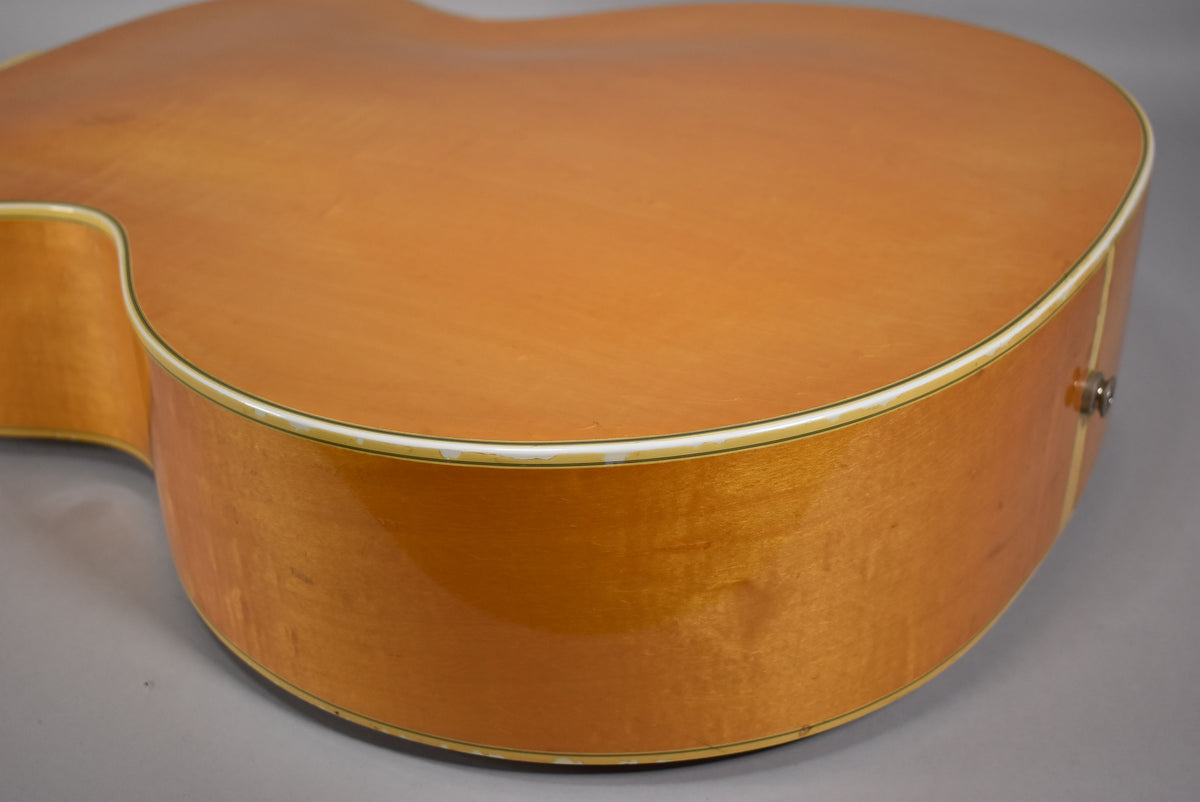 Close-up of the lower bout of a blonde acoustic guitar, showing the side and top with some finish wear along the binding.