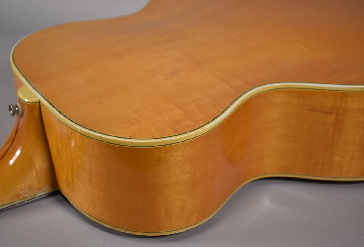 The upper bout and cutaway of a blonde acoustic guitar, showing light finish checking and a strap button.