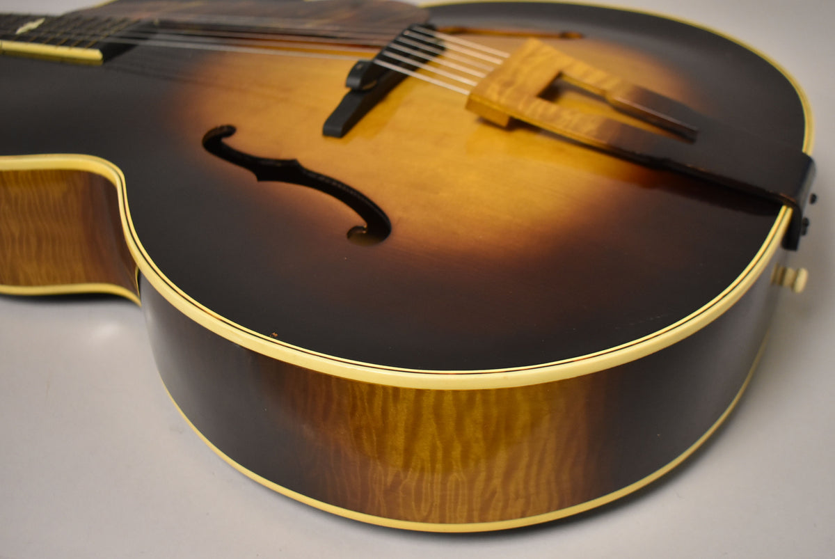 Close-up of the sunburst archtop's lower bout, showing the f-hole, wooden bridge, and flame maple sides with binding.