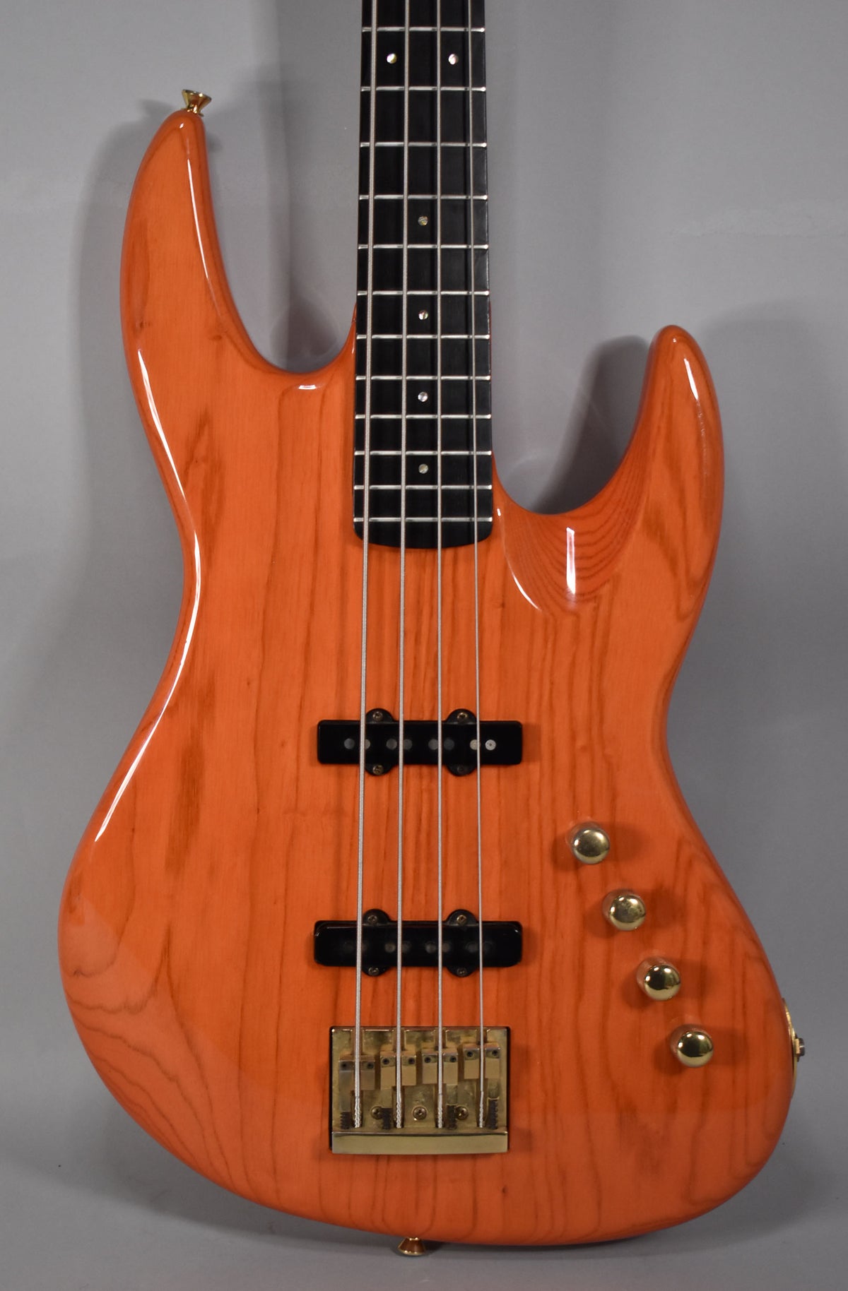 The translucent orange bass body, with visible wood grain, features gold hardware, two black pickups, and four gold control knobs.